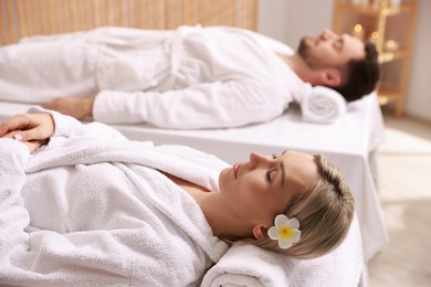 Photo of Couple in bathrobes lying on massage tables in spa salon, selective focus