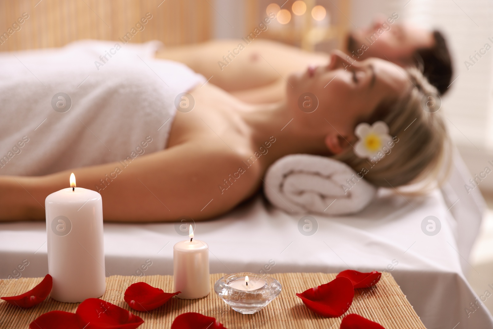 Photo of Couple lying on massage tables in spa salon, focus of petals and burning candles