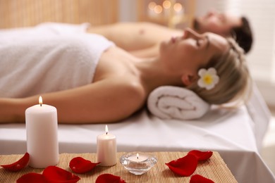 Photo of Couple lying on massage tables in spa salon, focus of petals and burning candles