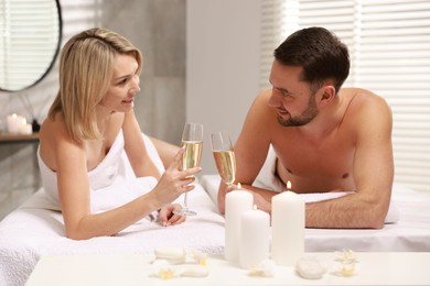 Photo of Happy couple with glasses of champagne lying on massage tables in spa salon