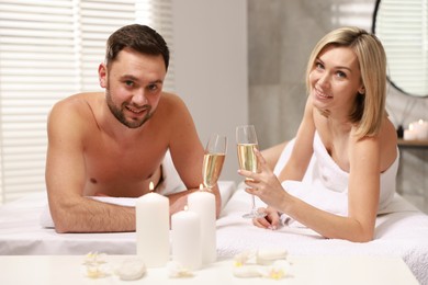 Photo of Happy couple with glasses of champagne lying on massage tables in spa salon