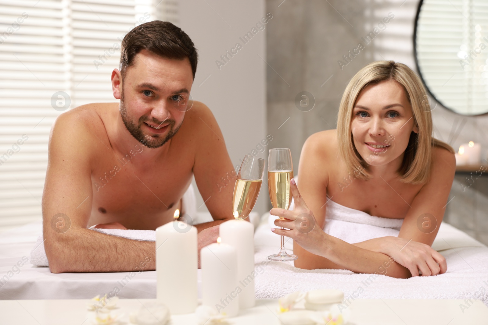 Photo of Happy couple with glasses of champagne lying on massage tables in spa salon