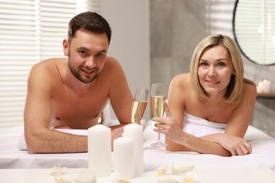 Photo of Happy couple with glasses of champagne lying on massage tables in spa salon