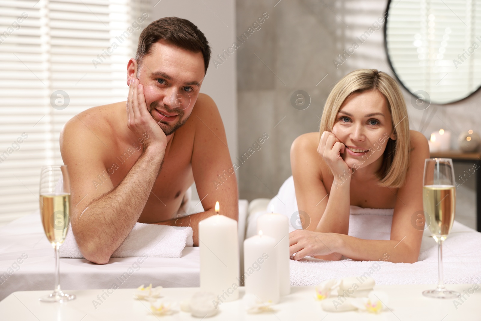 Photo of Happy couple with glasses of champagne lying on massage tables in spa salon