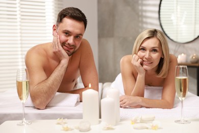 Photo of Happy couple with glasses of champagne lying on massage tables in spa salon