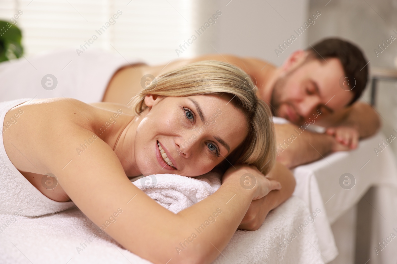 Photo of Happy couple lying on massage tables in spa salon, selective focus