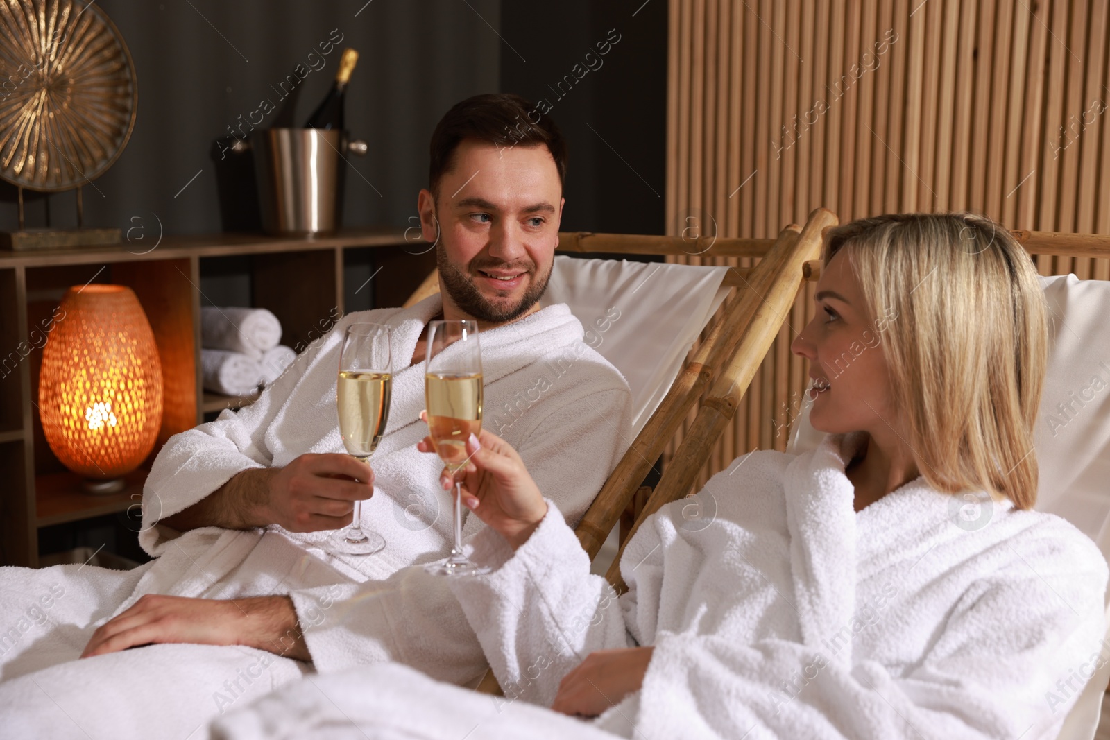 Photo of Happy couple in bathrobes with glasses of champagne relaxing in spa salon