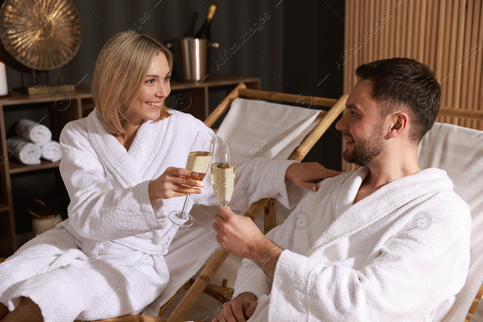 Photo of Happy couple in bathrobes with glasses of champagne relaxing in spa salon