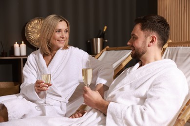 Photo of Happy couple in bathrobes with glasses of champagne relaxing in spa salon