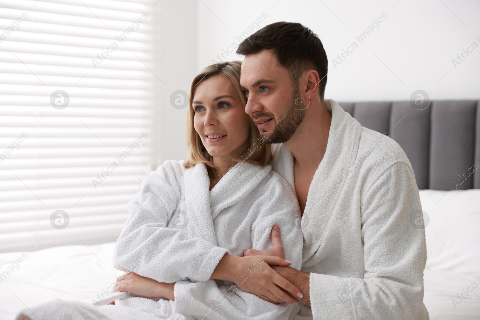 Photo of Spa. Happy couple in bathrobes sitting on bed indoors