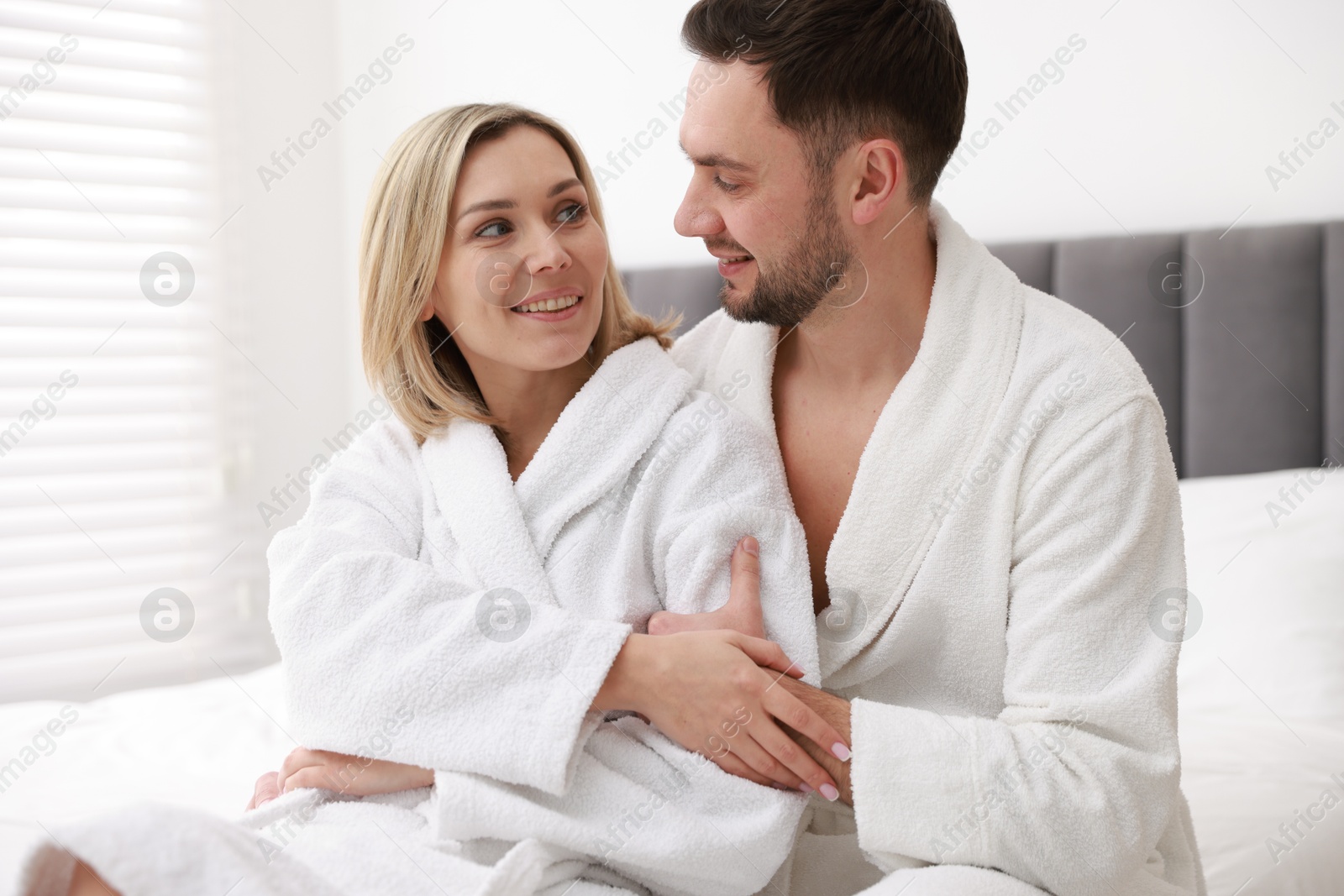 Photo of Spa. Happy couple in bathrobes sitting on bed indoors