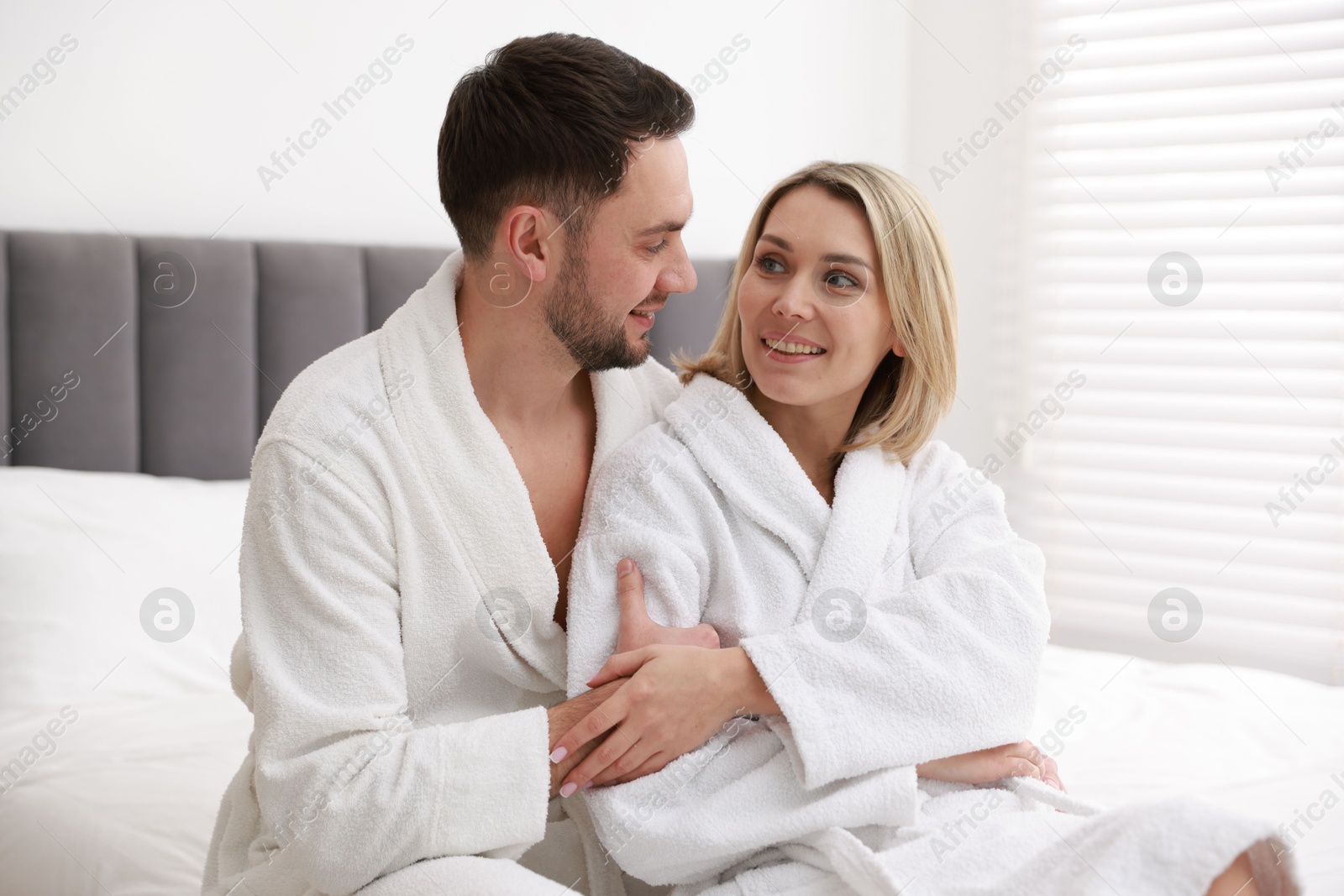 Photo of Spa. Happy couple in bathrobes sitting on bed indoors