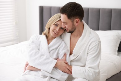 Photo of Spa. Happy couple in bathrobes sitting on bed indoors