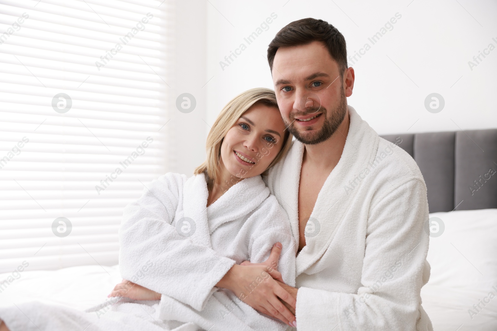 Photo of Spa. Happy couple in bathrobes sitting on bed indoors