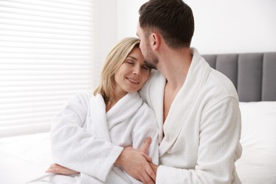 Photo of Spa. Happy couple in bathrobes sitting on bed indoors