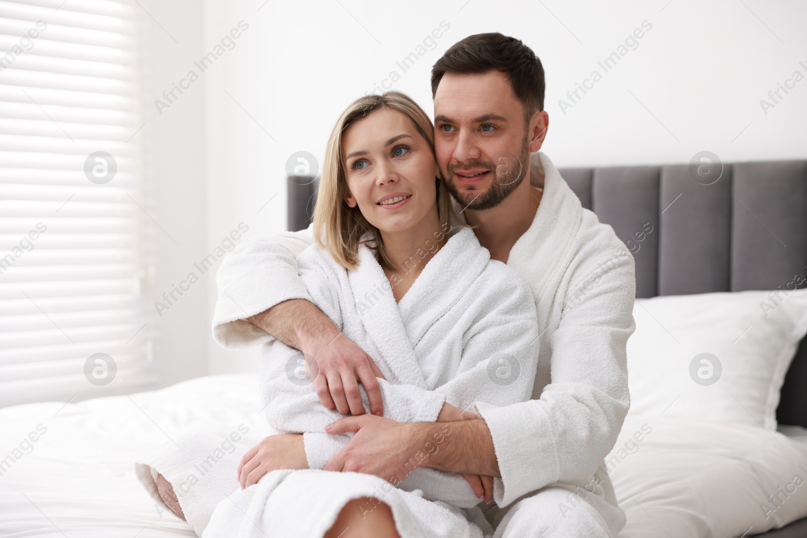 Photo of Spa. Happy couple in bathrobes sitting on bed indoors