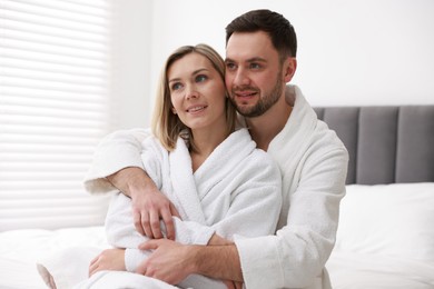 Photo of Spa. Happy couple in bathrobes sitting on bed indoors