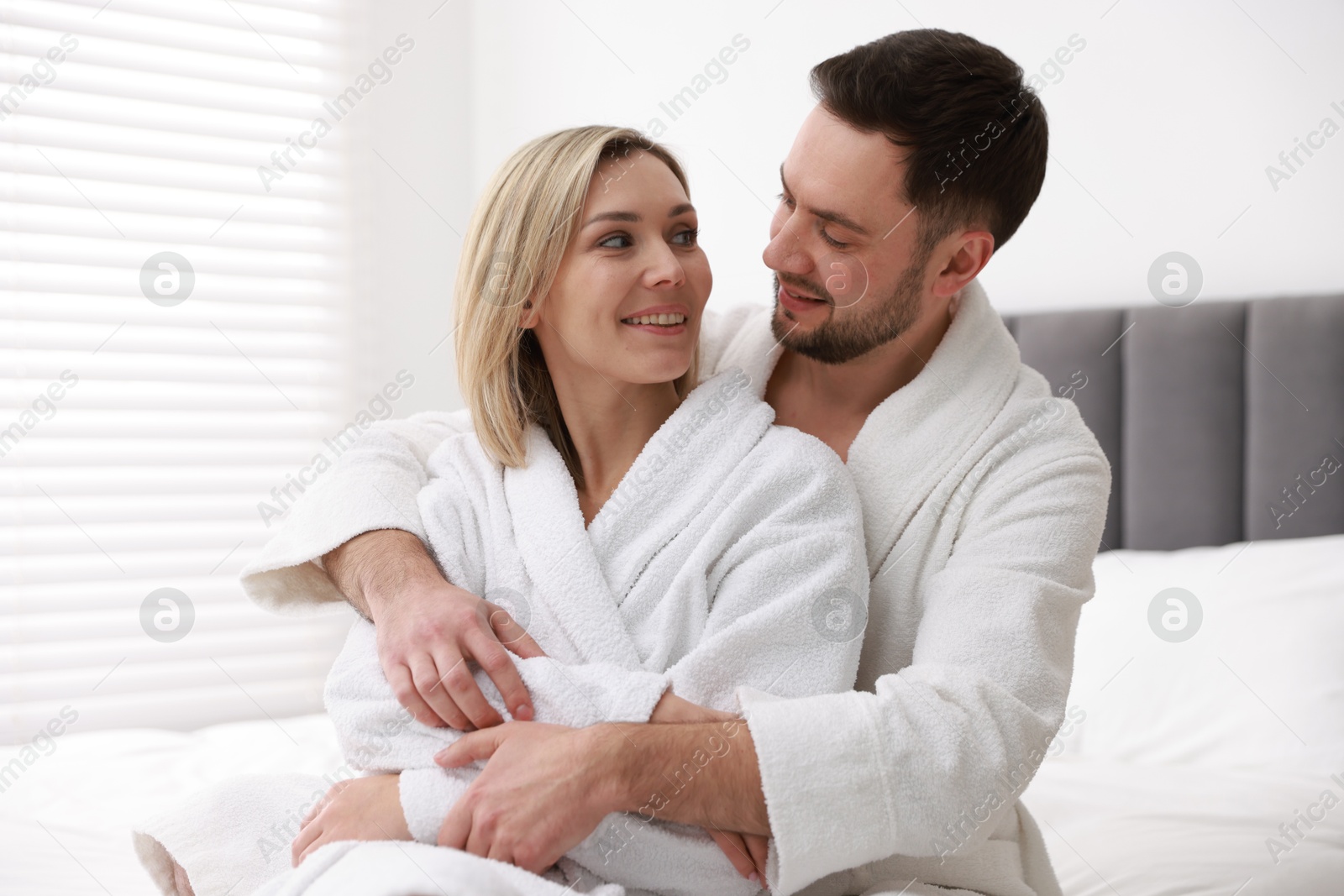 Photo of Spa. Happy couple in bathrobes sitting on bed indoors