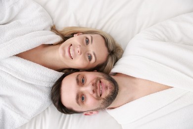 Photo of Spa. Happy couple in bathrobes lying on bed, top view