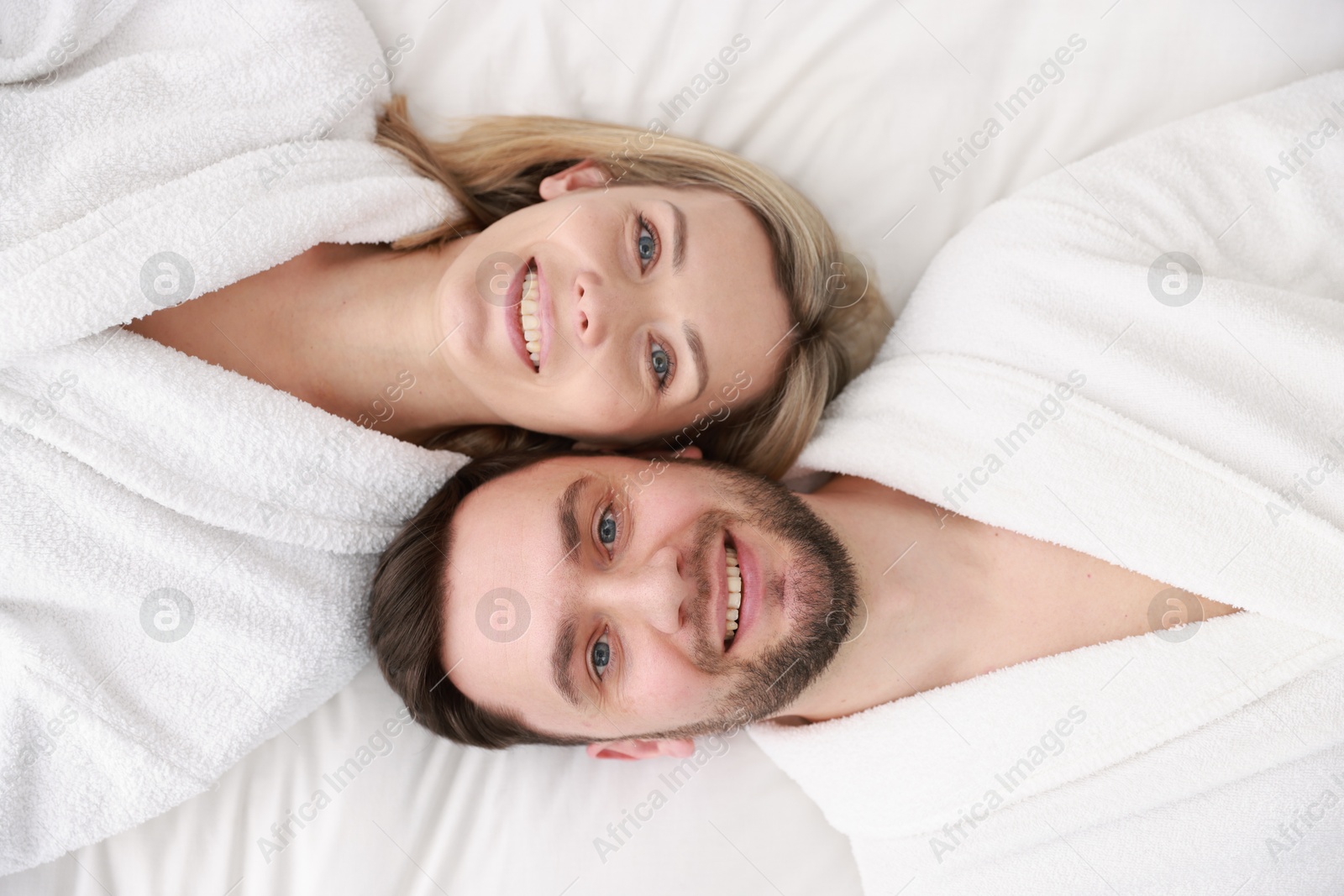 Photo of Spa. Happy couple in bathrobes lying on bed, top view