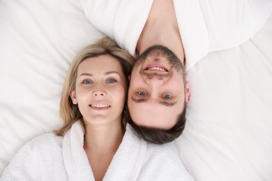 Photo of Spa. Happy couple in bathrobes lying on bed, top view