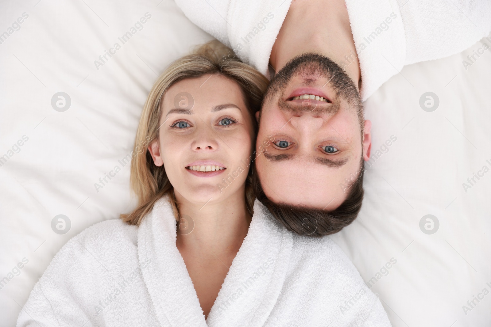 Photo of Spa. Happy couple in bathrobes lying on bed, top view