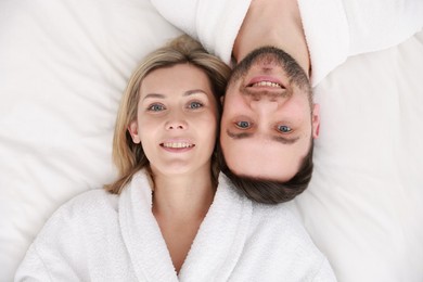 Photo of Spa. Happy couple in bathrobes lying on bed, top view