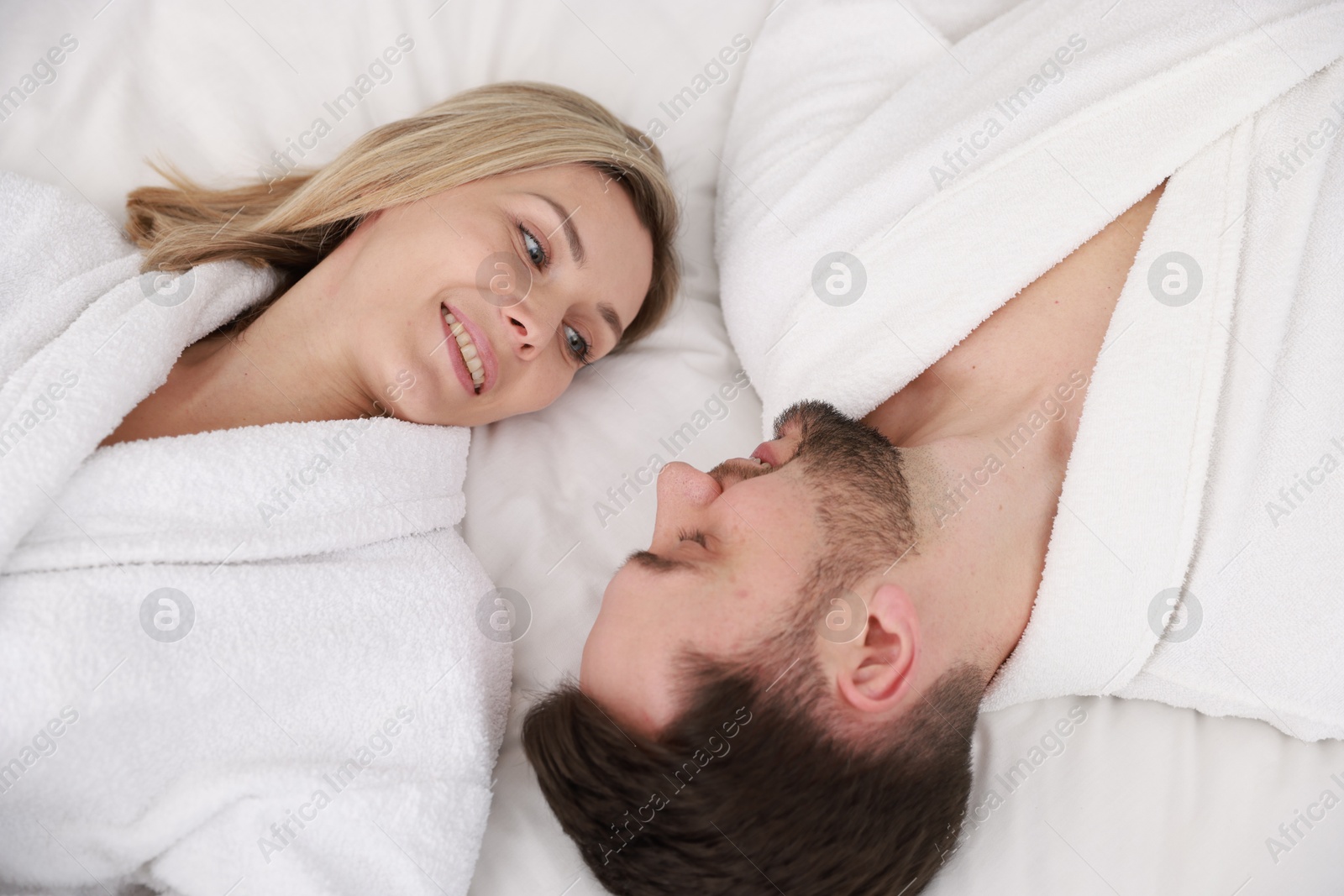 Photo of Spa. Happy couple in bathrobes lying on bed, above view