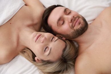 Photo of Spa. Happy couple lying on bed, above view