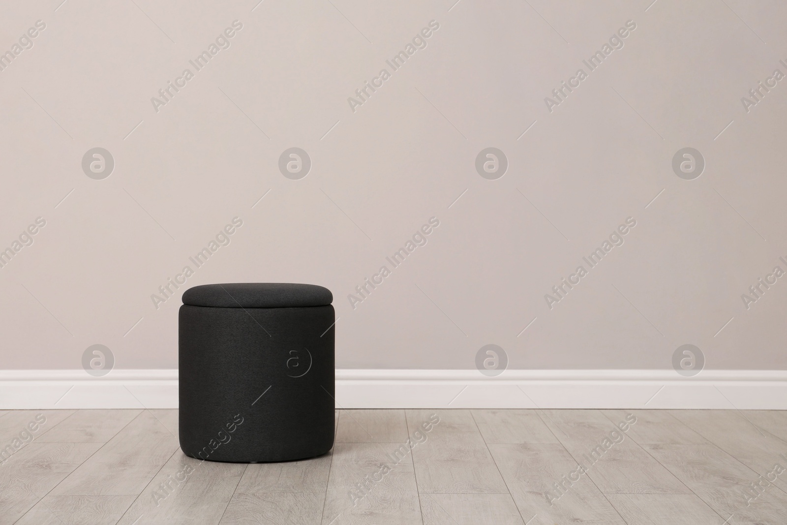 Photo of Stylish pouf near beige wall indoors. Space for text