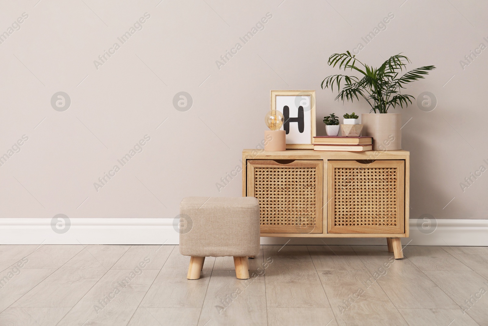 Photo of Stylish pouf and cabinet near beige wall indoors. Space for text