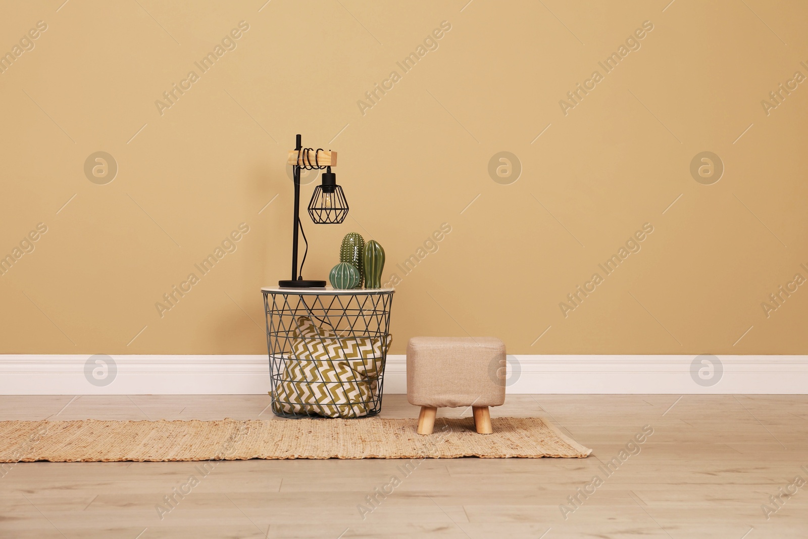 Photo of Stylish comfortable ottoman and lamp near beige wall indoors, space for text