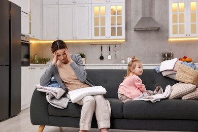 Photo of Housewife with her little daughter folding laundry on sofa at home