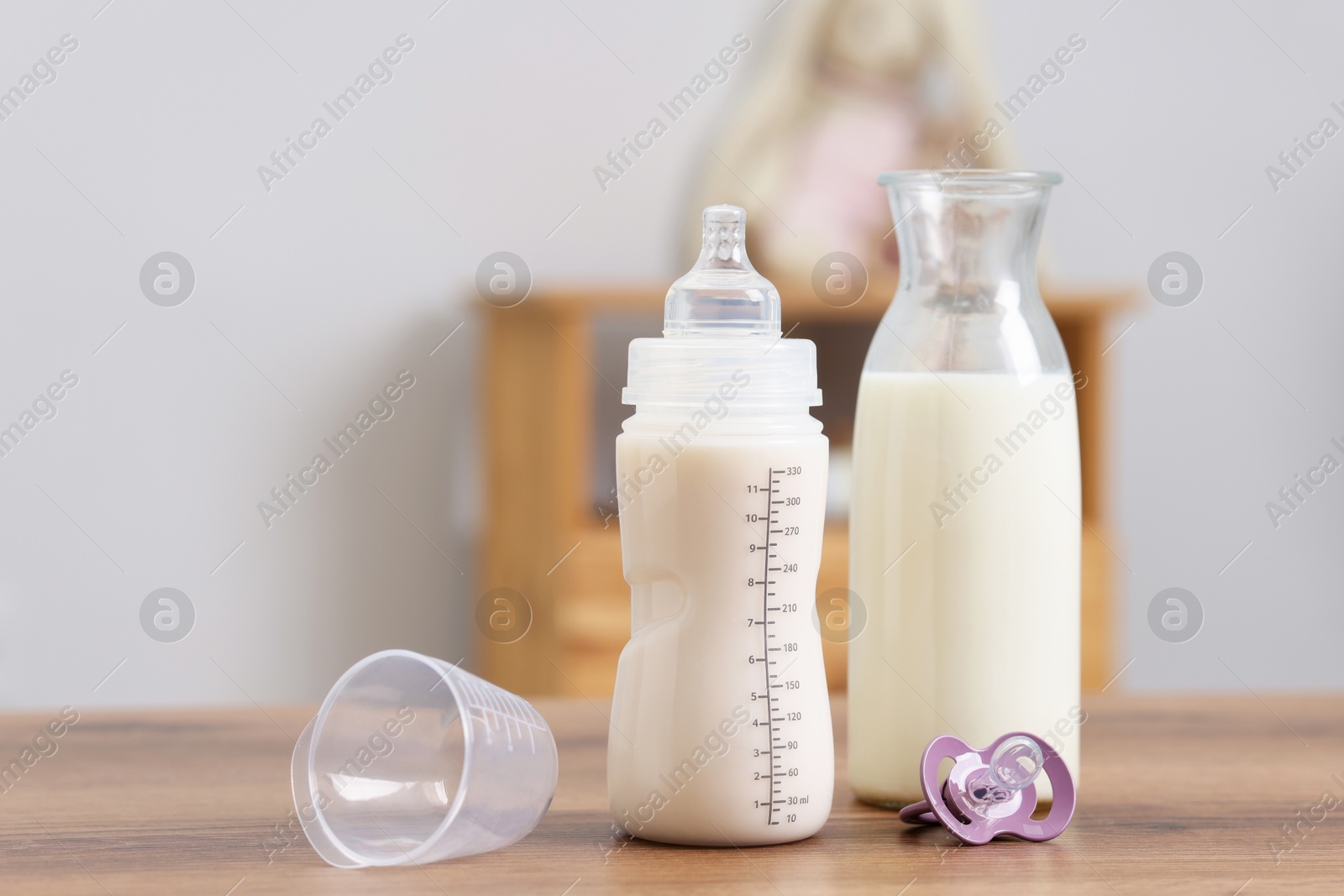 Photo of Milk in feeding bottle, jug and pacifier on wooden table indoors