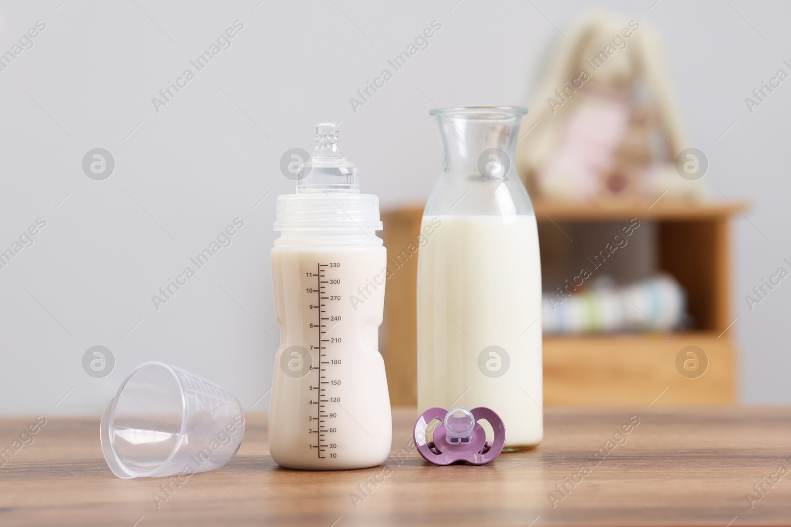 Photo of Milk in feeding bottle, jug and pacifier on wooden table indoors