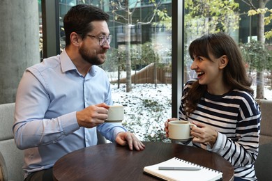 Photo of Happy colleagues talking during coffee break at wooden table in cafe