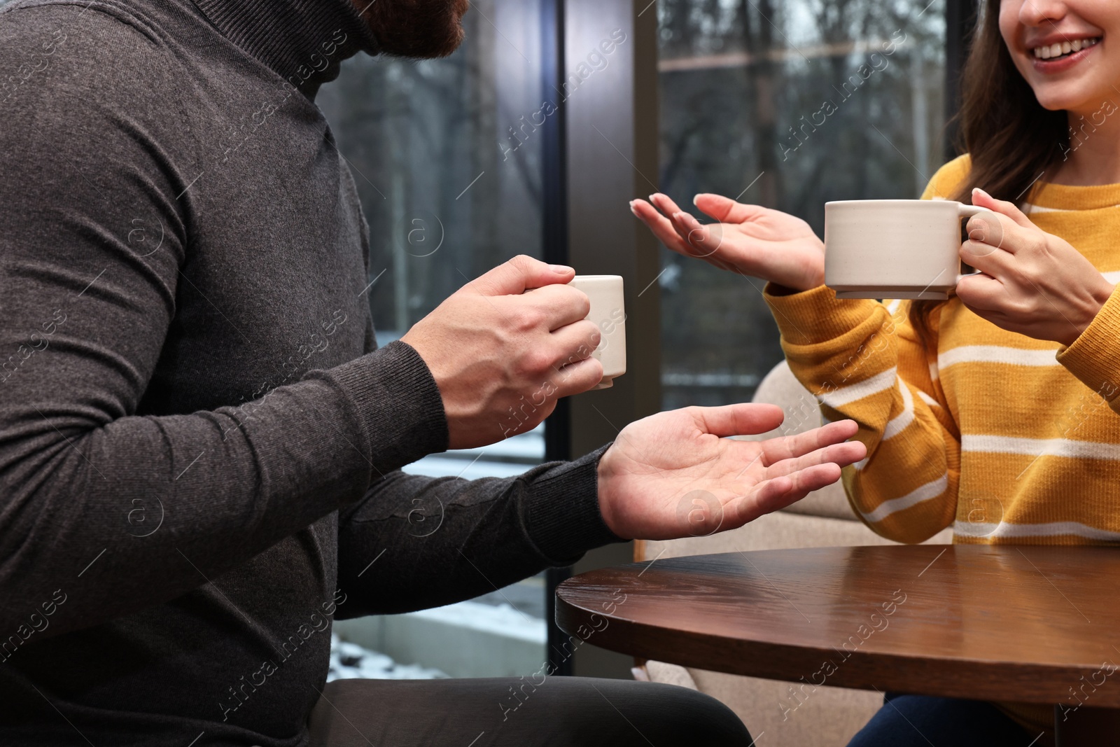 Photo of Colleagues talking during coffee break at wooden table in cafe, closeup