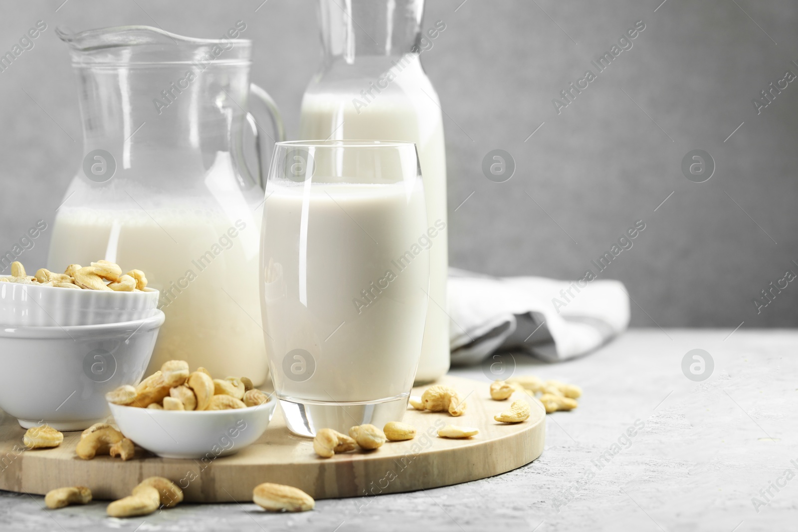 Photo of Glassware with fresh cashew milk and nuts on grey table, space for text