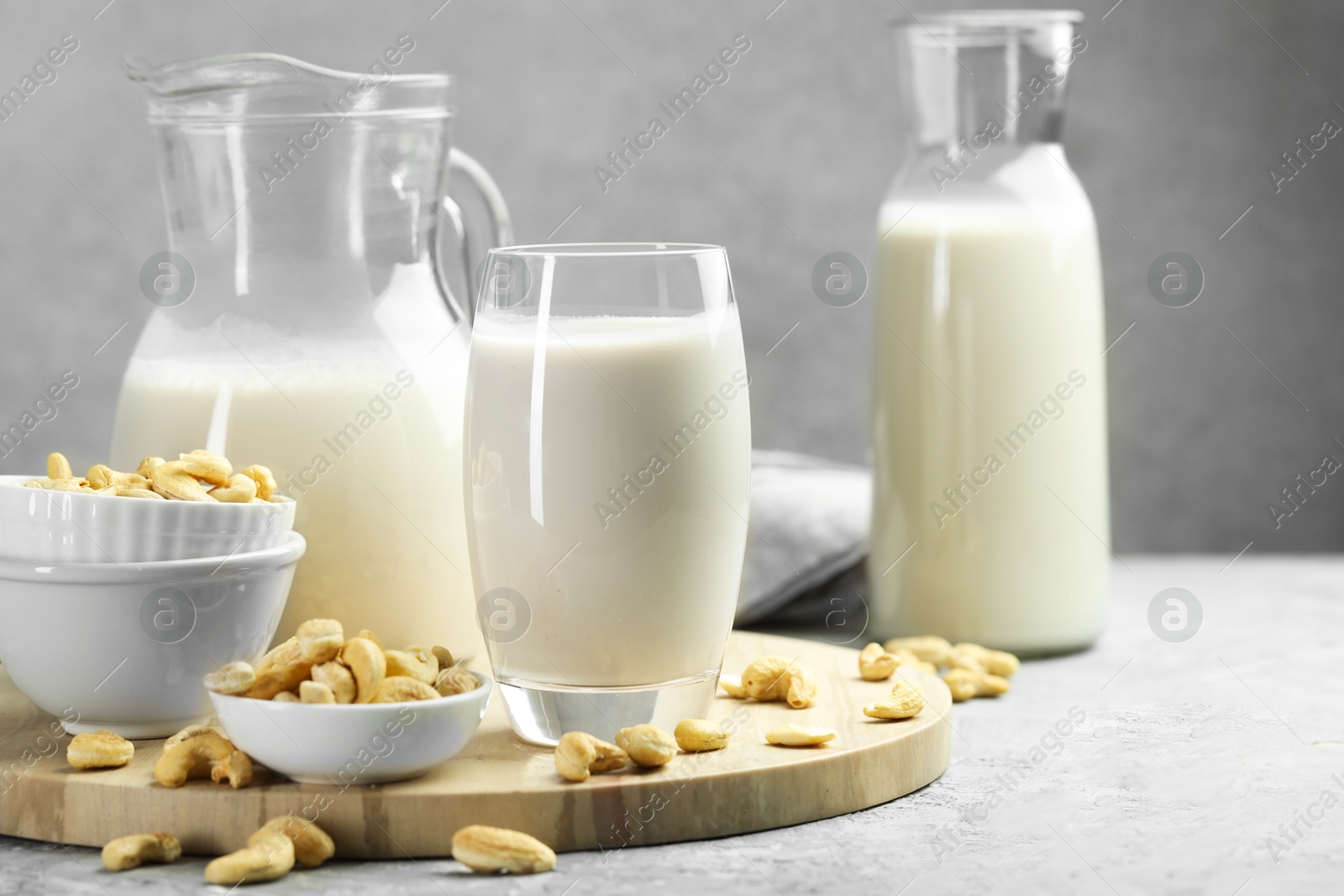 Photo of Glassware with fresh cashew milk and nuts on grey table, space for text