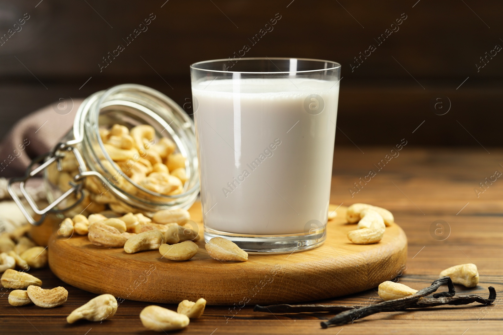 Photo of Fresh cashew milk in glass, nuts and vanilla pods on wooden table, closeup