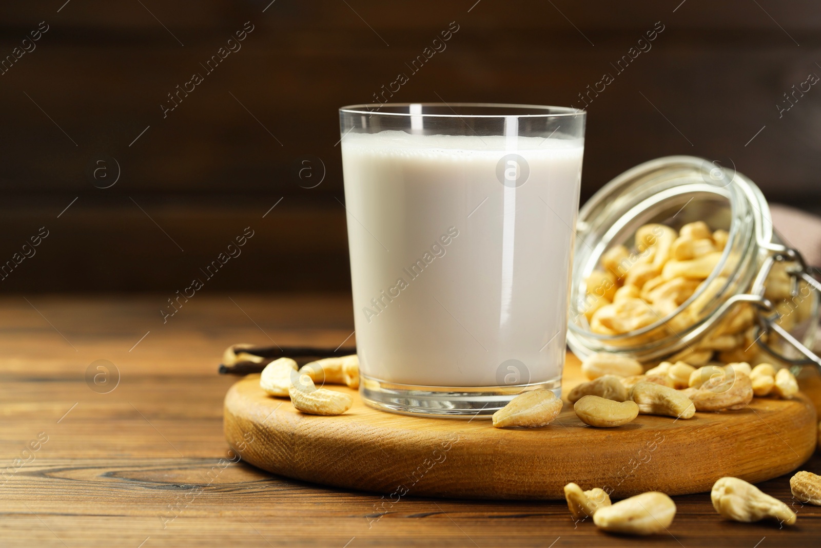 Photo of Fresh cashew milk in glass and nuts on wooden table, closeup. Space for text