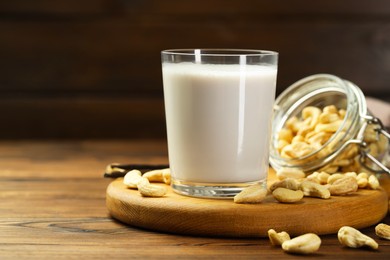 Photo of Fresh cashew milk in glass and nuts on wooden table, closeup. Space for text