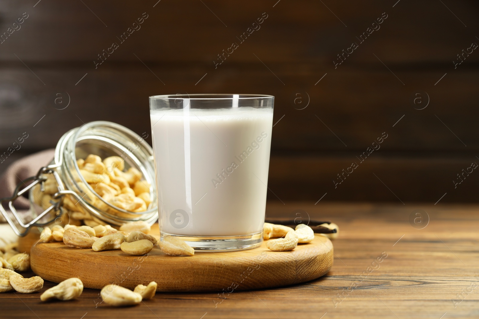 Photo of Fresh cashew milk in glass and nuts on wooden table, space for text