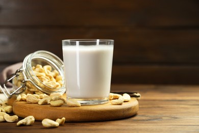 Photo of Fresh cashew milk in glass and nuts on wooden table, space for text