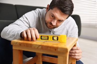 Photo of Man using level tool while repairing wooden stool at home, selective focus