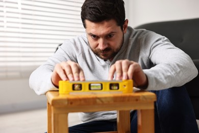 Photo of Man using level tool while repairing wooden stool at home, selective focus