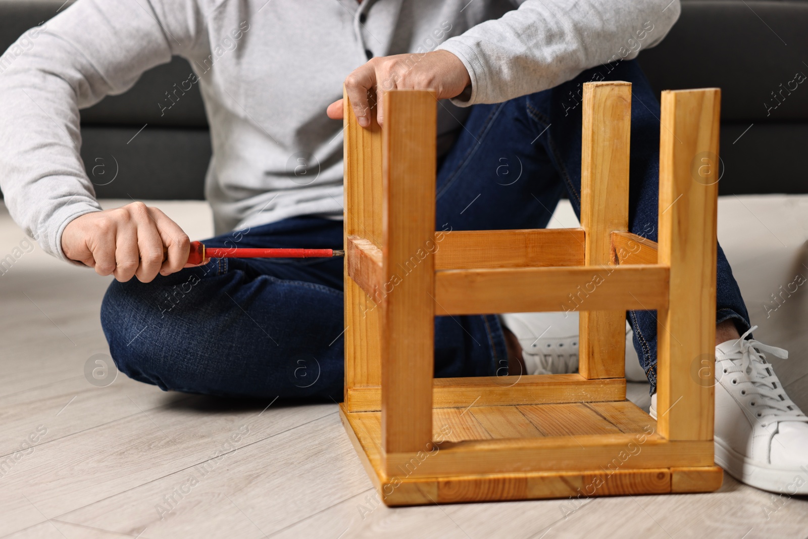 Photo of Man repairing wooden stool with screwdriver at home, closeup