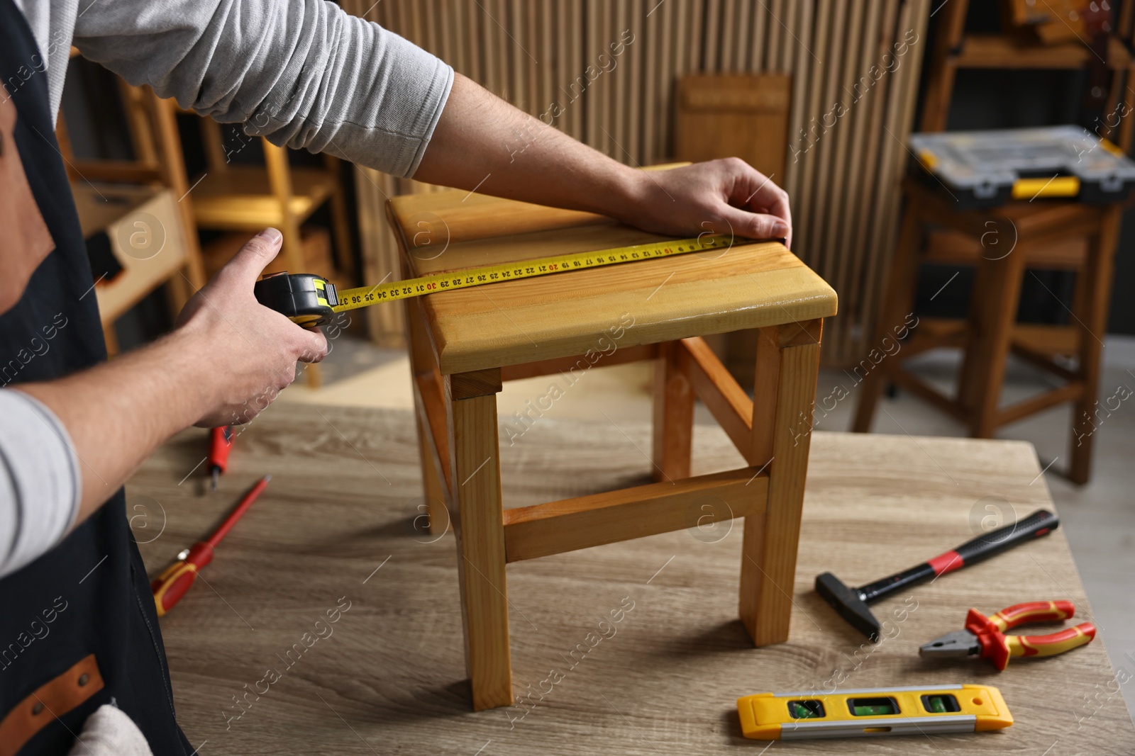 Photo of Repairman measuring wooden stool at table in workshop, closeup