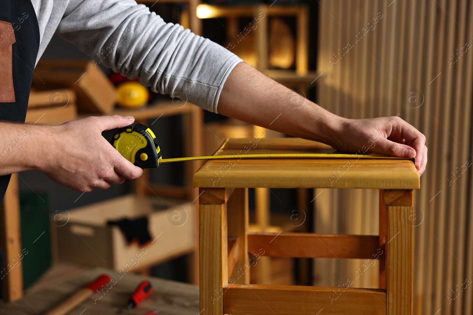 Photo of Repairman measuring wooden stool in workshop, closeup