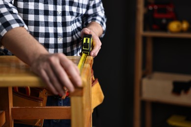 Photo of Repairman measuring wooden stool in workshop, closeup